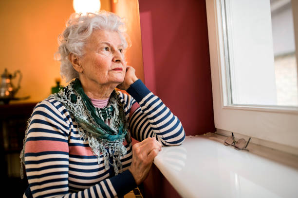 istock Sad alone senior woman looking through window at home 1044737010