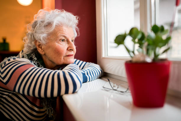 istock Sad alone senior woman looking through window 1044737166