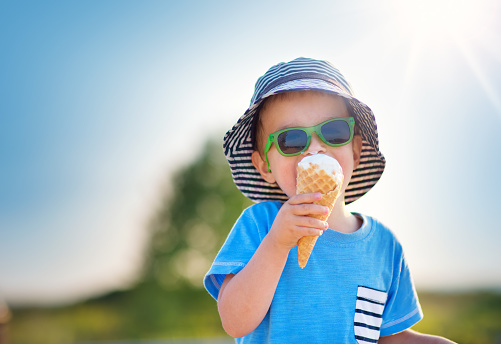 Happy child eating ice cream outdoors in summer. Portrait of a boy in sunglasses on sunny day