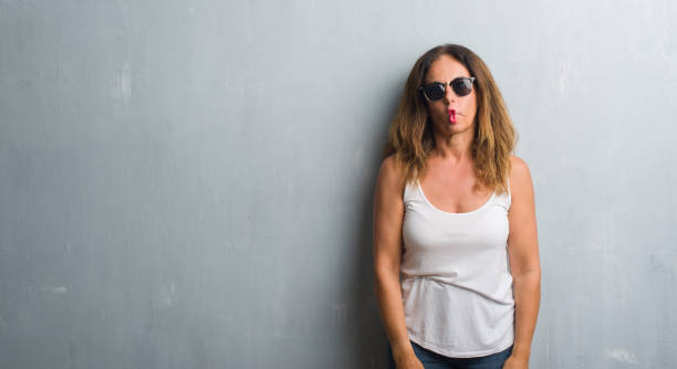 istock Middle age hispanic woman over grey wall wearing sunglasses making fish face with lips, crazy and comical gesture. Funny expression. 1044760724