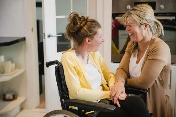 Mature mother is relaxing in the kitchen with her daughter who is in a wheelchair.