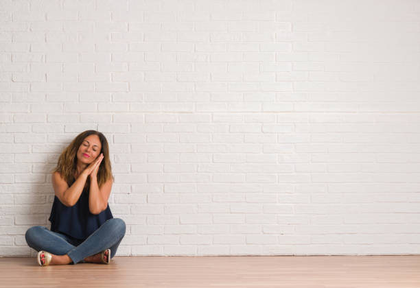 istock Middle age hispanic woman sitting on the floor over white brick wall sleeping tired dreaming and posing with hands together while smiling with closed eyes. 1044763942