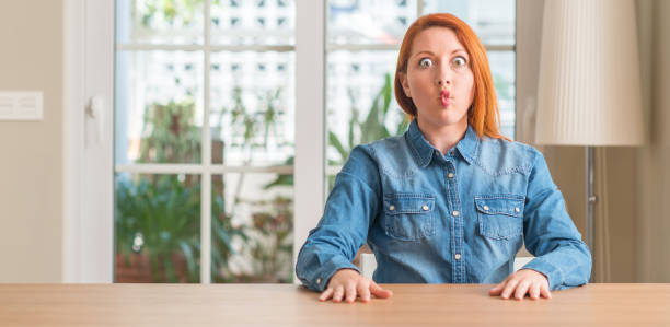 istock Redhead woman at home making fish face with lips, crazy and comical gesture. Funny expression. 1044768046