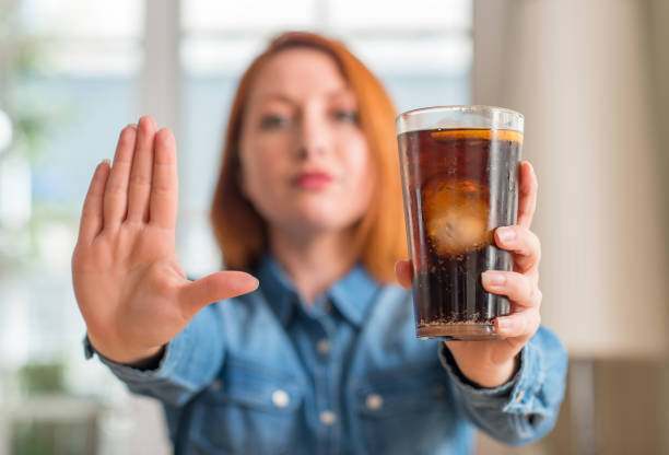 istock Redhead woman holding soda refreshment with open hand doing stop sign with serious and confident expression, defense gesture 1044768400