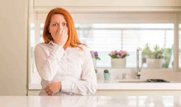 Redhead woman at kitchen smelling something stinky and disgusting, intolerable smell, holding breath with fingers on nose. Bad smells concept. Redhead woman at kitchen smelling something stinky and disgusting, intolerable smell, holding breath with fingers on nose. Bad smells concept. unpleasant smell stock pictures, royalty-free photos & images