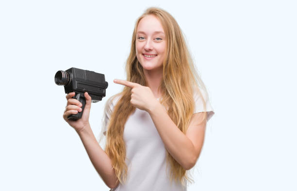 adolescent femme blonde tournage tenant une caméra super 8 très heureux pointant avec la main et des doigts - super 8 video camera photos et images de collection