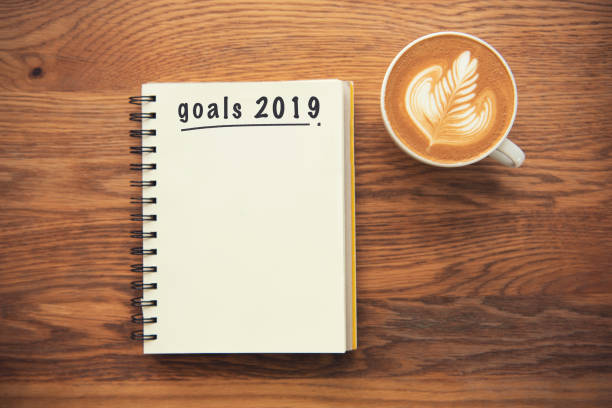 istock Coffee cup and notebook with goals 2019 on rustic desk from above, planner and checklist concept. 1044774104