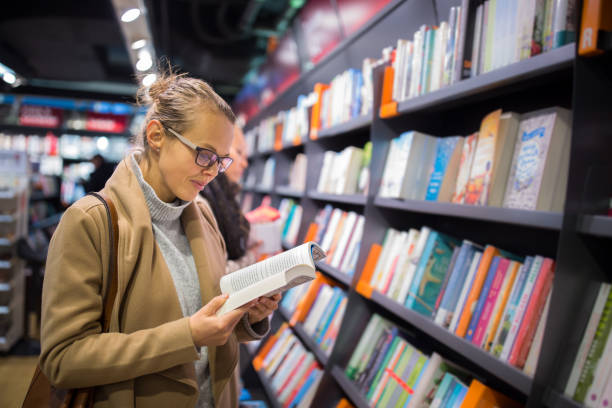 hübsche, junge frau, die wahl eines guten buches - buchhandlung stock-fotos und bilder