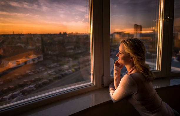 istock Smiling woman day dreaming while looking through the window at sunset. 1044782932