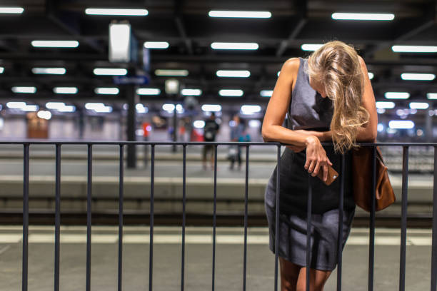 Exhausted overworked young female commuter waiting for her daily train in a modern trainstation, using her cellphone while waiting (color toned image)