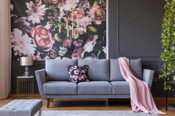 Real photo of a living room interior with a sofa, pillow, blanket and flowers on wallpaper