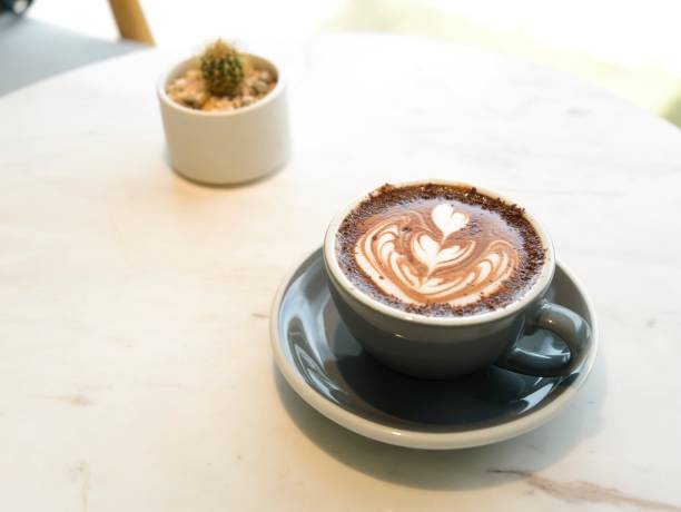 istock Hot chocolate latte art with dark color plate on white marble table with blur cactus plants 1044791430