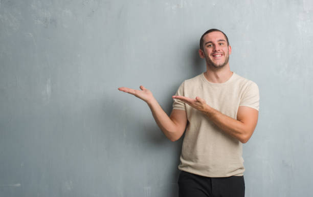 istock Young caucasian man over grey grunge wall amazed and smiling to the camera while presenting with hand and pointing with finger. 1044791818