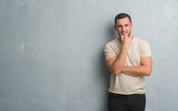 istock Young caucasian man over grey grunge wall looking confident at the camera with smile with crossed arms and hand raised on chin. Thinking positive. 1044791994