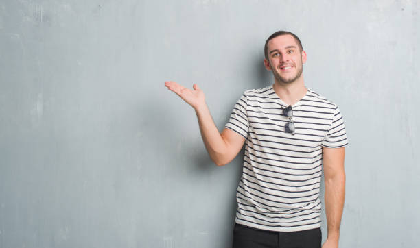 istock Young caucasian man over grey grunge wall smiling cheerful presenting and pointing with palm of hand looking at the camera. 1044799778