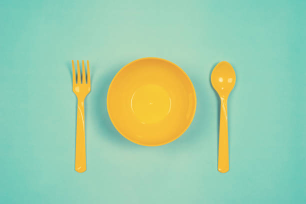 istock Set of empty yellow plastic tableware bowls, spoons and forks  isolated on green pastel background. Flat lay, Top view. Minimal style. 1044800220