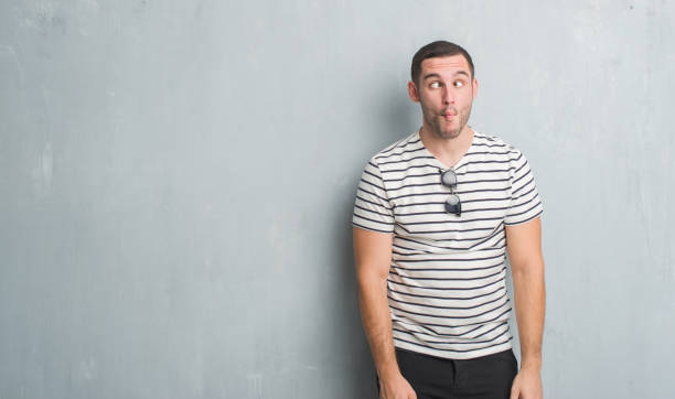 istock Young caucasian man over grey grunge wall making fish face with lips, crazy and comical gesture. Funny expression. 1044800300