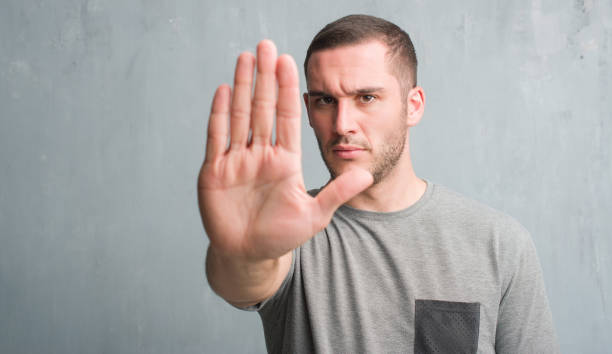 istock Young caucasian man over grey grunge wall with open hand doing stop sign with serious and confident expression, defense gesture 1044805504