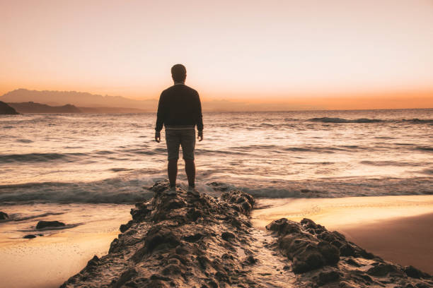 istock Rear view of young man at empty beach at sunset 1044807870
