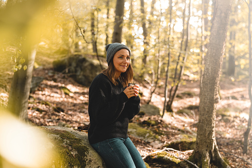 A beautiful woman is out in a forest in Sweden, picking mushrooms and stopping for a break to drink coffee on a sunny autumn day.