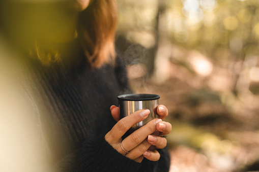 A beautiful woman is out in a forest in Sweden, picking mushrooms and stopping for a break to drink coffee on a sunny autumn day.