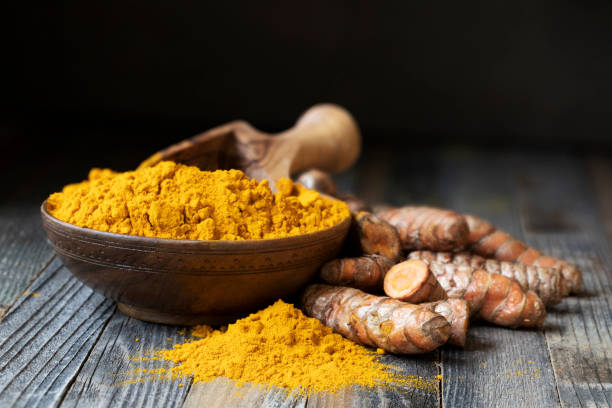 Turmeric Powder Still Life Scoop in bowl of turmeric powder with turmeric roots and copy space. turmeric stock pictures, royalty-free photos & images