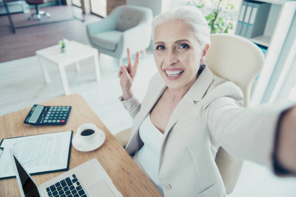 istock Grey-haired beautiful stylish old funky lady executive worker taking self picture, showing v-sign, work place work station 1044820178