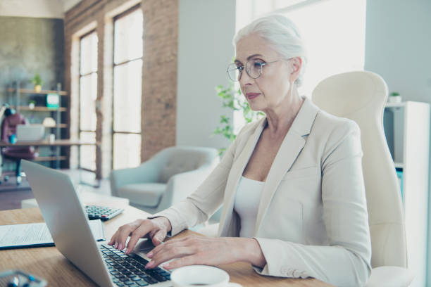 istock Gray-haired beautiful stylish professional serious old lady executive worker typing email letter on laptop at work place work station 1044821066