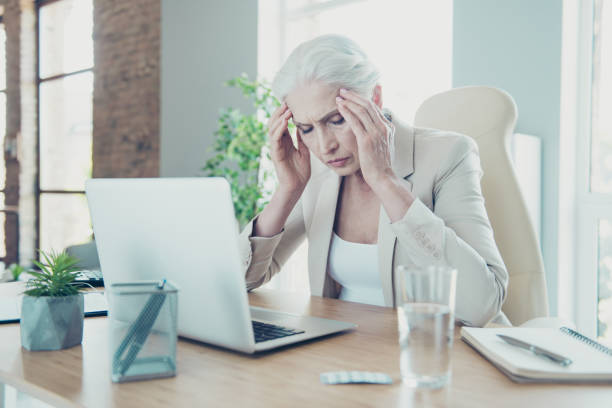 istock Gray-haired beautiful stylish old unhappy sad lady executive worker suffering from disease, migraine at work place work station, taking pills 1044821224