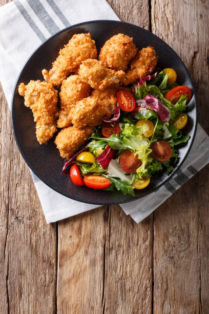 istock deep-fried chicken wings in breadcrumbs and fresh vegetable close-up. Vertical top view 1044827780