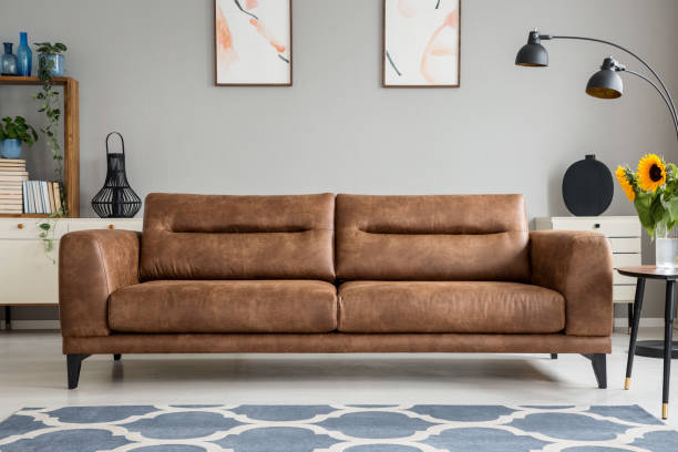 istock Patterned blue carpet in front of brown leather sofa in grey living room interior with posters. Real photo 1044842218