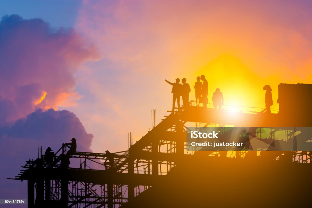 Silhouette of Engineer and worker on building site, construction site with clipping path at sunset in evening time. Construction Site Stock Photo