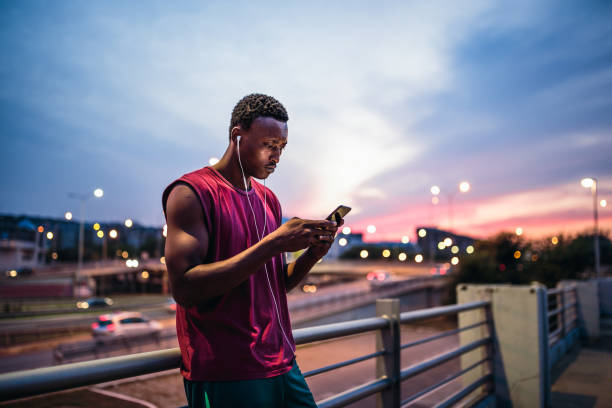 jóvenes hombres africanos descansando después al aire libre de la formación, mediante teléfono móvil - running jogging urban scene city life fotografías e imágenes de stock