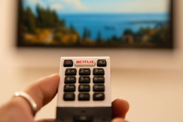 TV Remote Control with Netflix Button Ortigia, Italy - August 23, 2018: A hand holding television remote control with dedicated Netflix button in front of defocused smart tv television show stock pictures, royalty-free photos & images