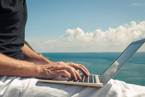 Male hands typing on a laptop with seascape background