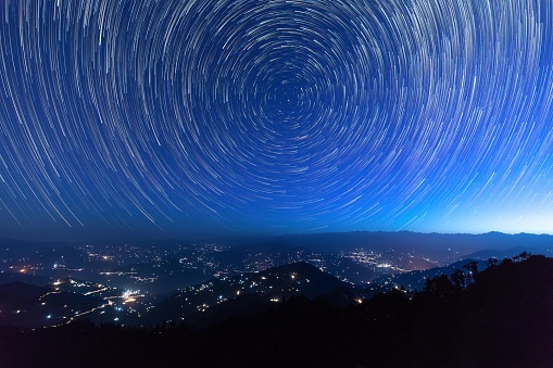 Night sky star trails around the North star with city lights in the background taken from the top of a hill in himalayas