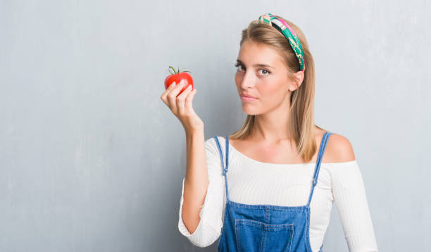 istock Beautiful young woman over grunge grey wall eating fresh tomato with a confident expression on smart face thinking serious 1044860888