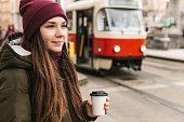 A girl drinks coffee from a disposable cup on the street in Prague near the tram stop.