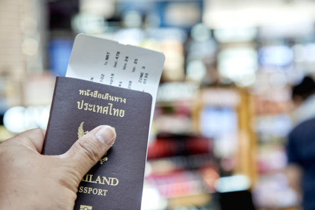 istock Man Left Hand Holding Thailand Passport with Airport Flight Schedule blurred 1044870282