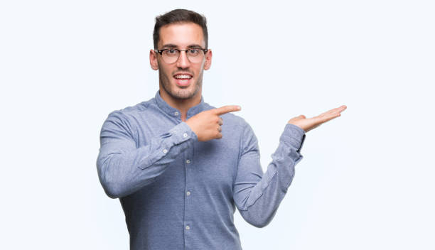 istock Handsome young elegant man wearing glasses amazed and smiling to the camera while presenting with hand and pointing with finger. 1044878858