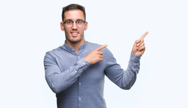 istock Handsome young elegant man wearing glasses smiling and looking at the camera pointing with two hands and fingers to the side. 1044878922