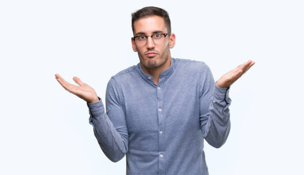 istock Handsome young elegant man wearing glasses clueless and confused expression with arms and hands raised. Doubt concept. 1044878932