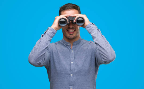 istock Handsome young man looking through binoculars with a happy face standing and smiling with a confident smile showing teeth 1044879284