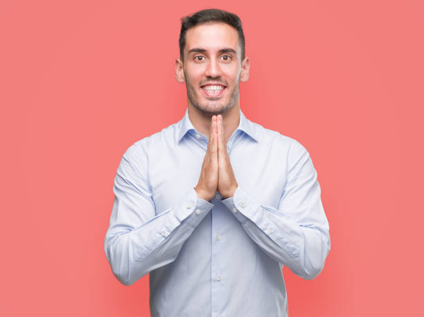 istock Handsome young businessman praying with hands together asking for forgiveness smiling confident. 1044880404