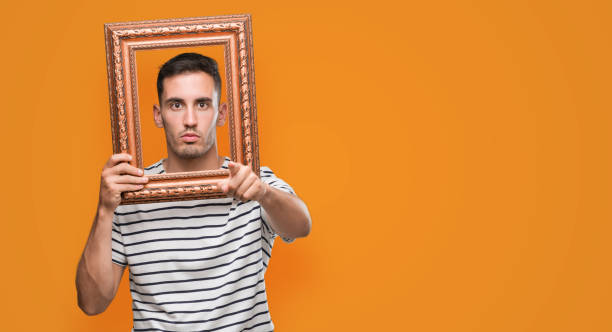 istock Handsome young man looking through vintage art frame pointing with finger to the camera and to you, hand sign, positive and confident gesture from the front 1044883282