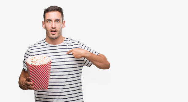 istock Handsome young man eating popcorn with surprise face pointing finger to himself 1044883412