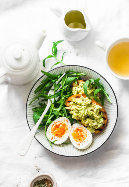 saludable desayuno o merienda - huevo, rúcula ensalada y aguacate tostada sobre un fondo claro, vista superior - salad breakfast cooked eggs fotografías e imágenes de stock