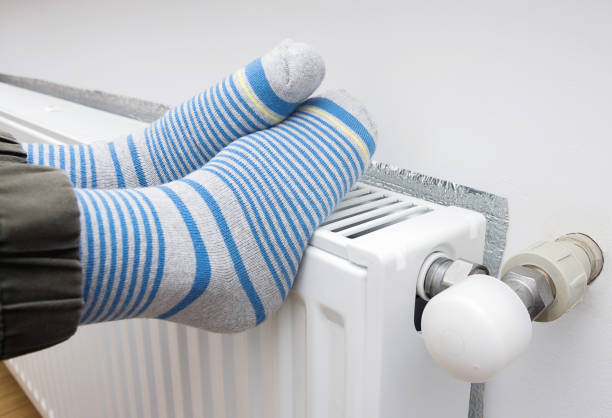 a child in warm winter socks warms his feet on the heater. - lubrication infection imagens e fotografias de stock