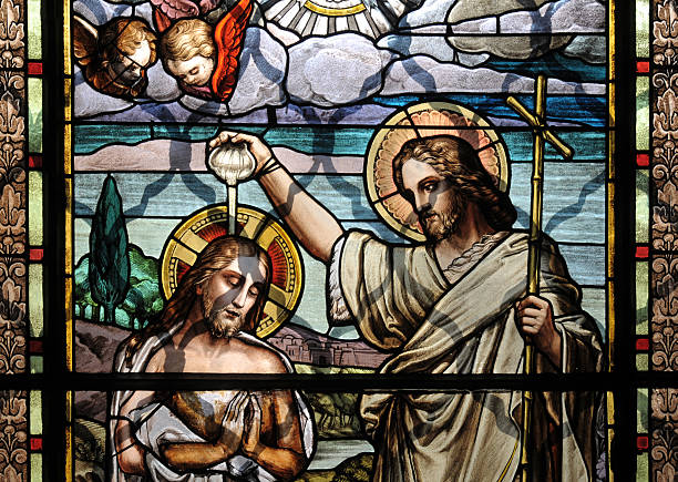 Colorful mosaic glass art of the Baptism of Jesus Jesus Christ baptism by Saint John the Baptist on an old stained glass window decoration in Sappada's Church (Belluno) Italy. baptism photos stock pictures, royalty-free photos & images
