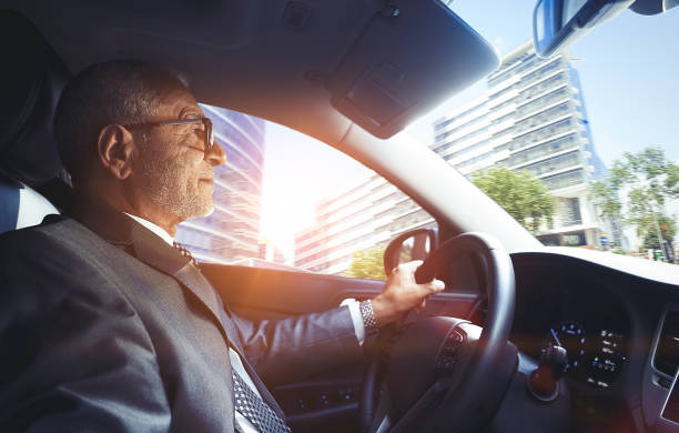 Senior businessman driving car in downtown district from interior view stock photo